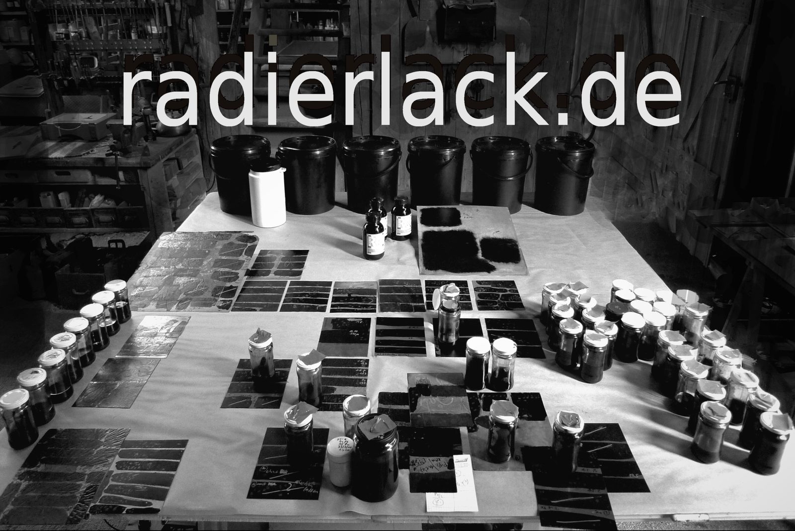 Atelier-Tisch mit Radierplatten und Gebinden des R&P Radierlacks, darüber der Schriftzug radierlack.de